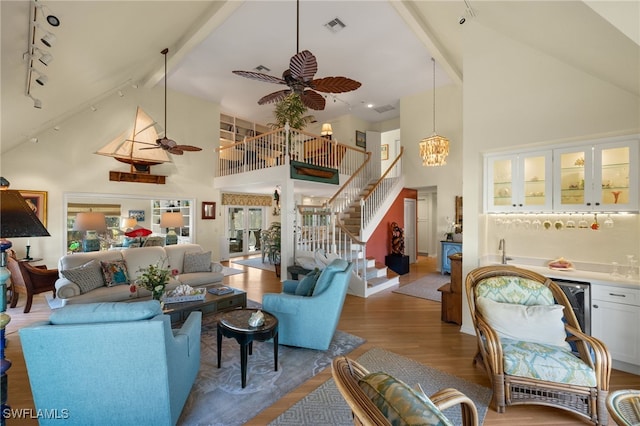 living room featuring wood-type flooring, bar area, high vaulted ceiling, beamed ceiling, and ceiling fan with notable chandelier