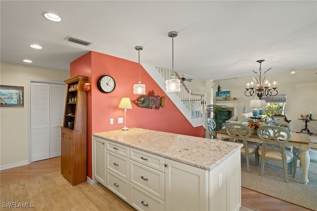 kitchen with hanging light fixtures, white cabinetry, light stone counters, and light wood-type flooring