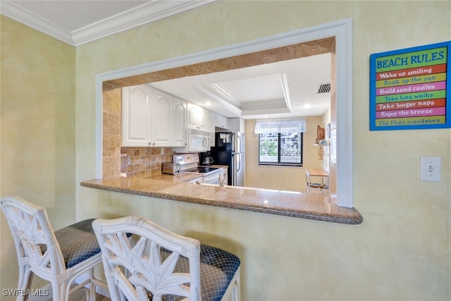 kitchen featuring white cabinetry, decorative backsplash, ornamental molding, a raised ceiling, and white appliances