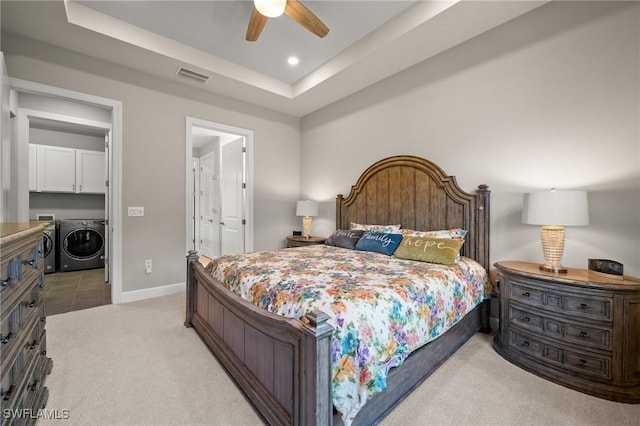 bedroom with light colored carpet, visible vents, baseboards, independent washer and dryer, and a raised ceiling