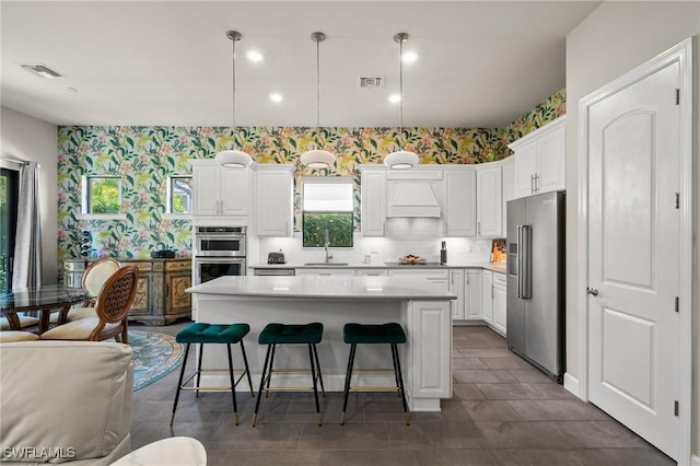 kitchen with wallpapered walls, appliances with stainless steel finishes, a center island, custom exhaust hood, and a sink