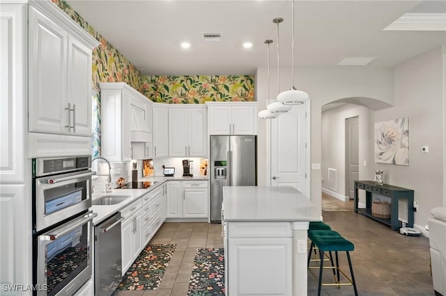 kitchen with arched walkways, appliances with stainless steel finishes, light countertops, white cabinetry, and a sink