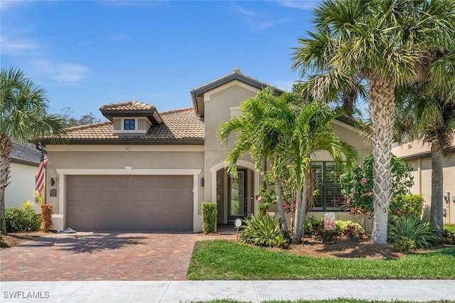 mediterranean / spanish-style home featuring a garage, decorative driveway, a tile roof, and stucco siding