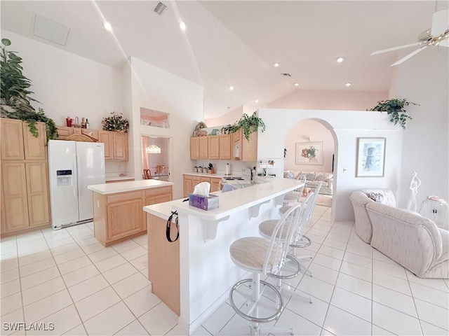 kitchen with a kitchen bar, a center island, light tile patterned floors, kitchen peninsula, and white fridge with ice dispenser