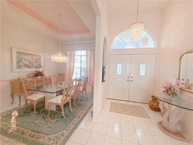 foyer entrance featuring a notable chandelier, light tile patterned floors, a raised ceiling, and a high ceiling