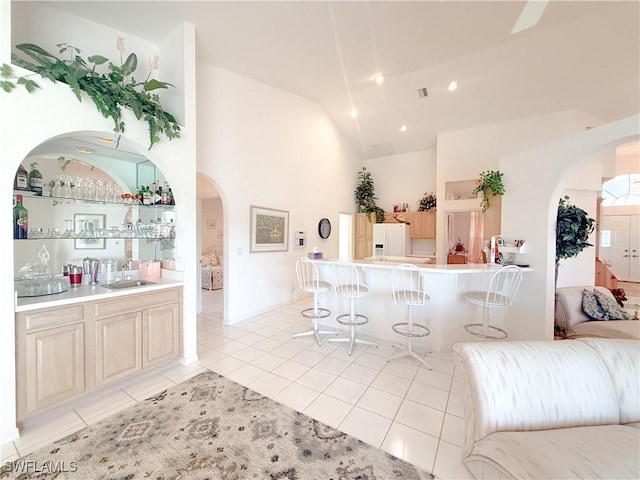 interior space featuring sink, light tile patterned floors, white fridge with ice dispenser, a kitchen bar, and light brown cabinets