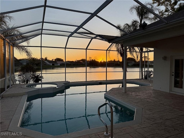 pool at dusk featuring a water view, an in ground hot tub, a patio area, and glass enclosure