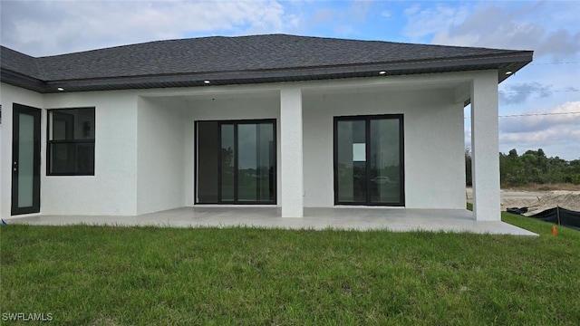 rear view of property with a patio area, a shingled roof, a lawn, and stucco siding