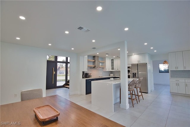 kitchen with a kitchen bar, white cabinetry, stainless steel fridge, a kitchen island, and wall chimney range hood