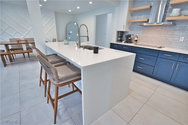 kitchen with a breakfast bar, range hood, an island with sink, sink, and backsplash