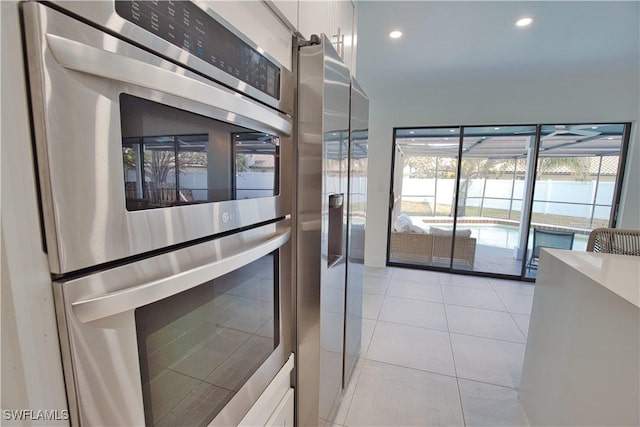 kitchen with stainless steel appliances, light tile patterned flooring, and white cabinets