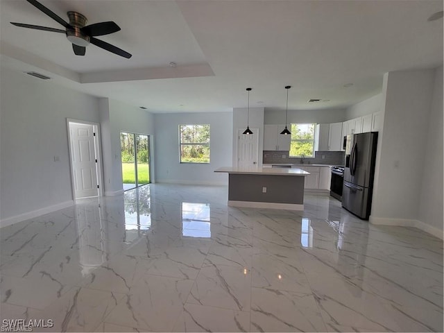 kitchen with hanging light fixtures, stainless steel appliances, a tray ceiling, white cabinets, and a kitchen island