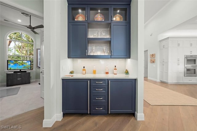 bar with hardwood / wood-style flooring, blue cabinetry, ceiling fan, double oven, and backsplash