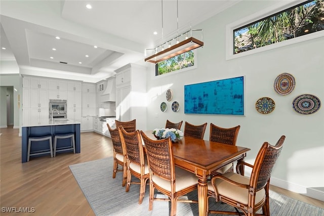 dining room featuring sink, a raised ceiling, and light wood-type flooring