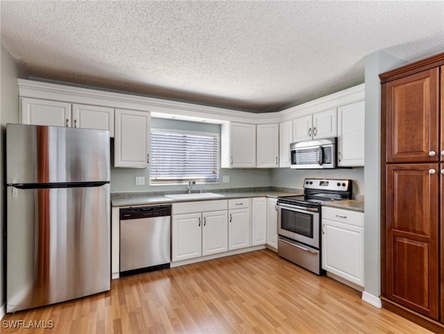 kitchen with sink, stainless steel appliances, white cabinets, and light wood-type flooring