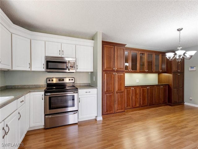 kitchen with white cabinetry, decorative light fixtures, light hardwood / wood-style flooring, a notable chandelier, and stainless steel appliances