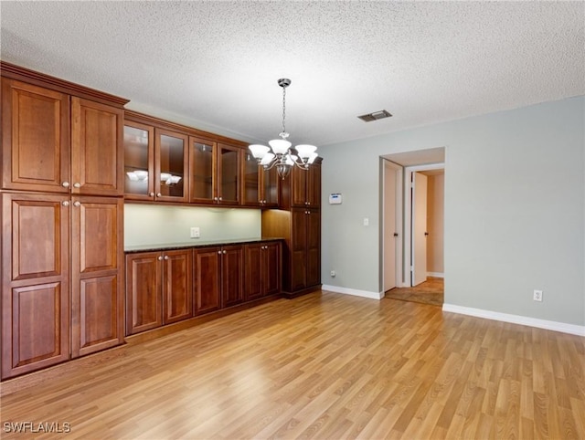 kitchen with decorative light fixtures, a textured ceiling, light hardwood / wood-style flooring, and a notable chandelier