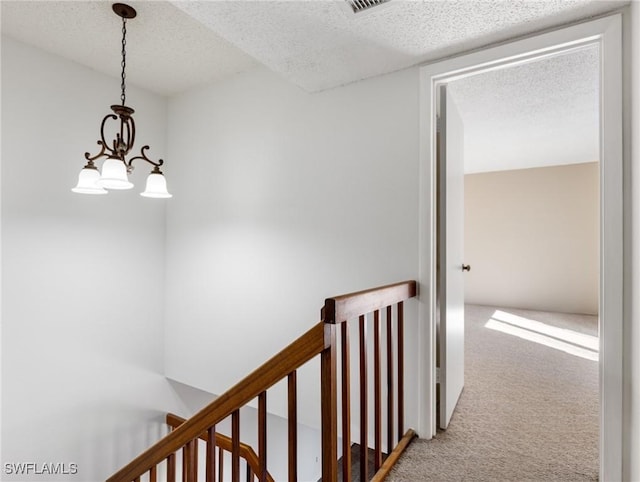 corridor featuring a notable chandelier, a textured ceiling, and carpet