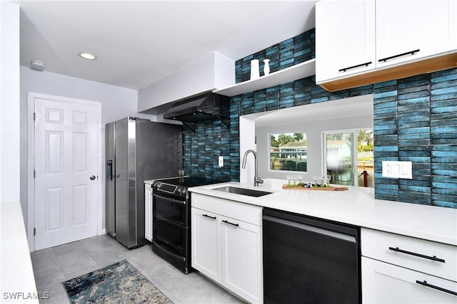 kitchen featuring wall chimney range hood, black appliances, sink, and white cabinets