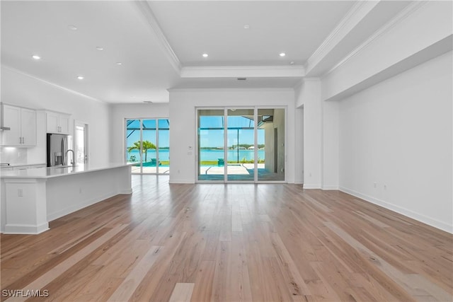 unfurnished living room featuring sink, ornamental molding, a tray ceiling, and light hardwood / wood-style floors