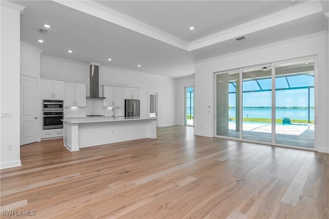 kitchen with white cabinetry, an island with sink, stainless steel fridge with ice dispenser, a water view, and wall chimney range hood