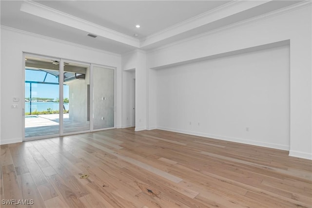 unfurnished room with a tray ceiling, crown molding, light wood-type flooring, and a water view