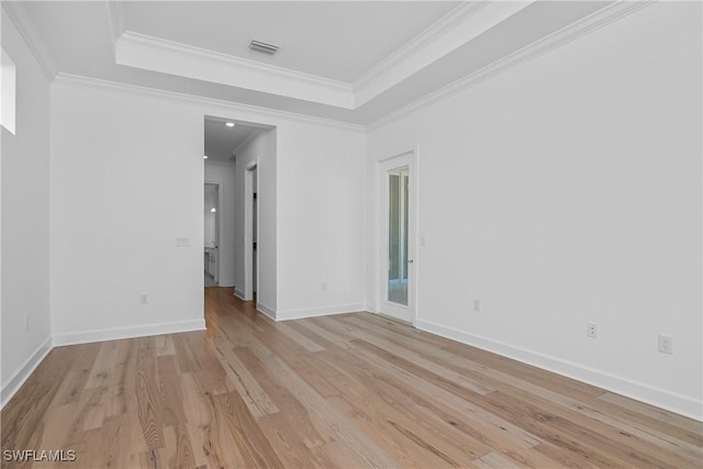 empty room with ornamental molding, a raised ceiling, and light hardwood / wood-style flooring