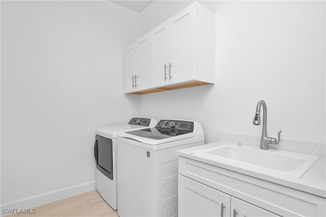 laundry room featuring cabinets, sink, washing machine and dryer, and light hardwood / wood-style flooring