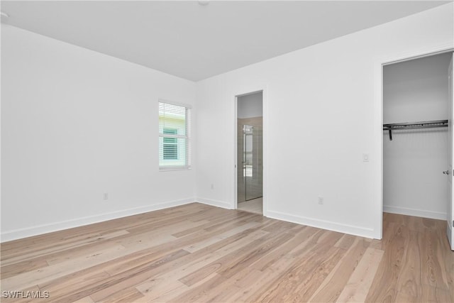 unfurnished bedroom with a spacious closet, light hardwood / wood-style floors, and a closet