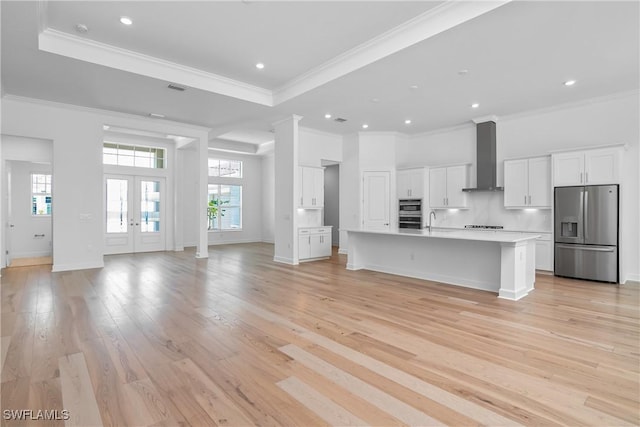 unfurnished living room with sink, light hardwood / wood-style floors, a tray ceiling, crown molding, and french doors