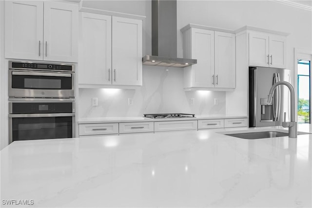 kitchen with white cabinetry, wall chimney range hood, light stone countertops, and appliances with stainless steel finishes