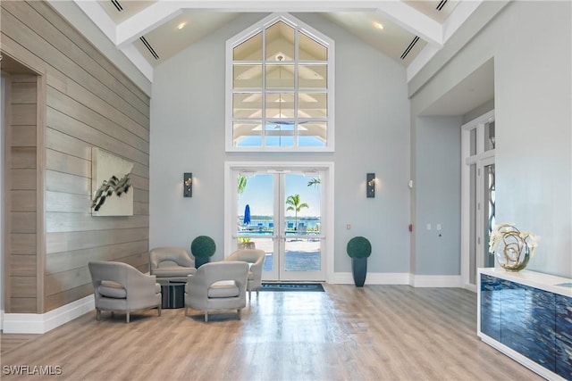 sitting room featuring french doors, wood walls, high vaulted ceiling, light wood-type flooring, and beamed ceiling