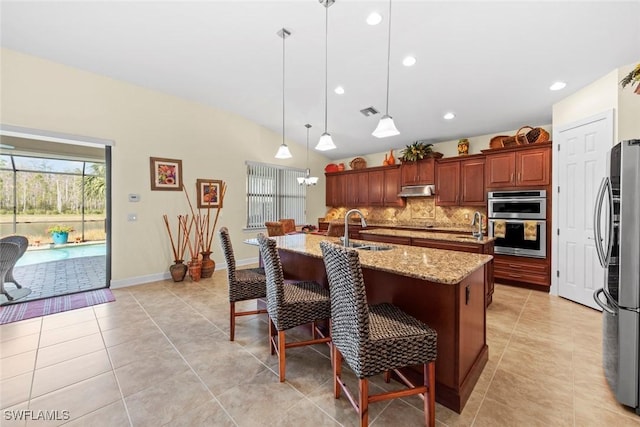 kitchen featuring appliances with stainless steel finishes, decorative light fixtures, an island with sink, sink, and a breakfast bar area