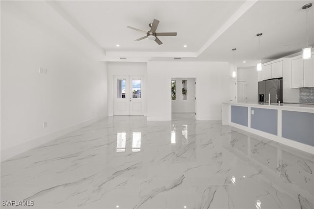 unfurnished living room featuring a raised ceiling, ceiling fan, and french doors