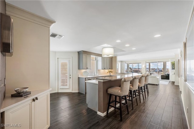 kitchen with gray cabinets, a kitchen island, sink, a kitchen bar, and dark wood-type flooring