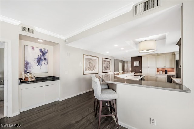 kitchen featuring dark wood-type flooring, ornamental molding, kitchen peninsula, and a kitchen bar