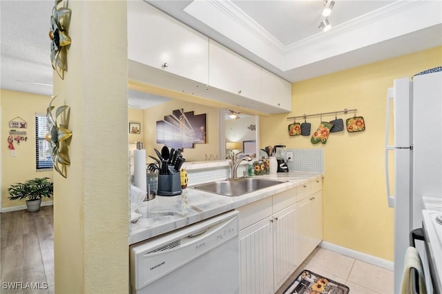 kitchen with white appliances, a sink, light countertops, crown molding, and a raised ceiling