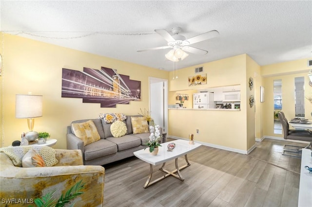 living area with a ceiling fan, baseboards, wood finished floors, visible vents, and a textured ceiling