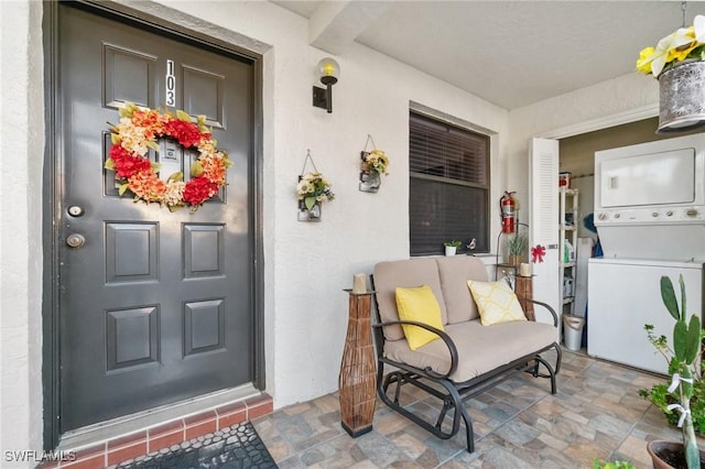 doorway to property featuring stucco siding and stacked washer / dryer