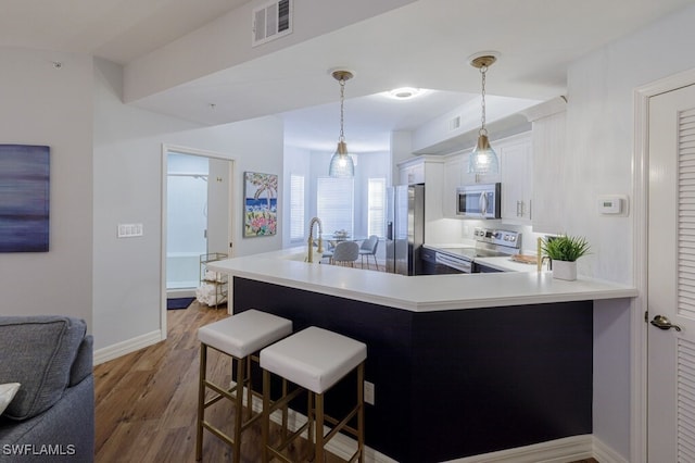 kitchen with pendant lighting, appliances with stainless steel finishes, white cabinetry, a kitchen bar, and kitchen peninsula