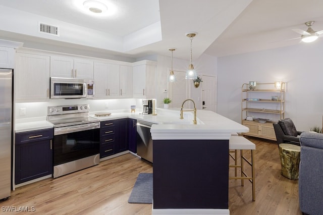 kitchen with decorative light fixtures, white cabinetry, a breakfast bar area, kitchen peninsula, and stainless steel appliances