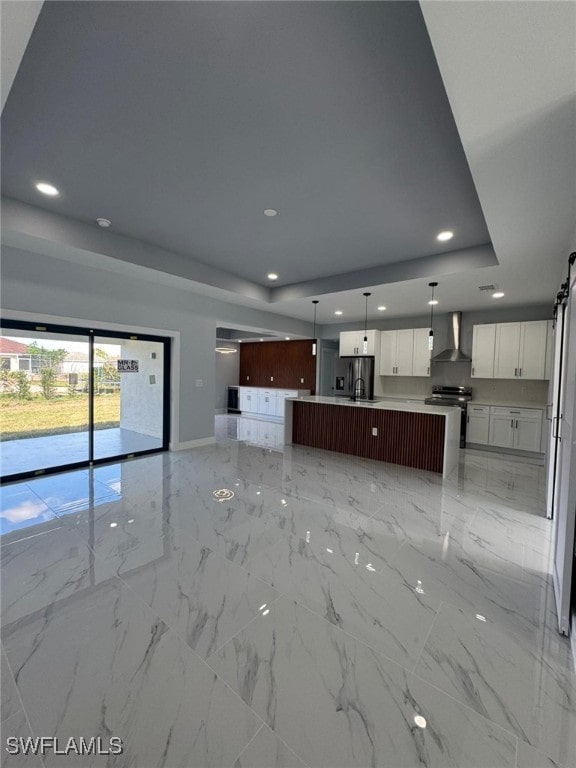 kitchen featuring a kitchen island with sink, white cabinets, stainless steel electric stove, a raised ceiling, and wall chimney exhaust hood