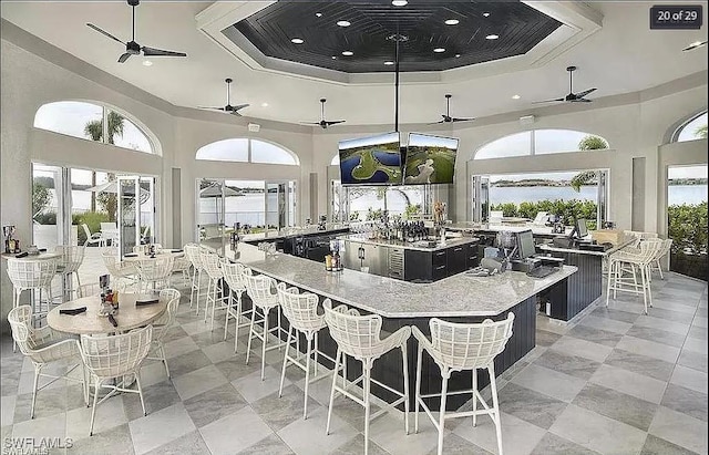 kitchen with a high ceiling, a tray ceiling, ceiling fan, a kitchen breakfast bar, and a large island