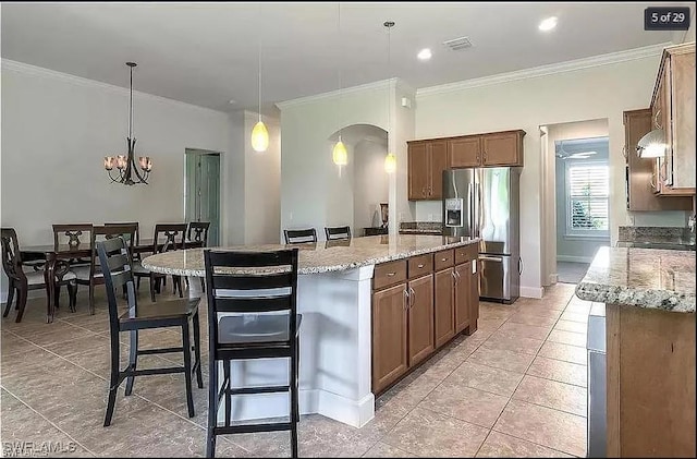 kitchen with a breakfast bar area, a center island, ornamental molding, decorative light fixtures, and stainless steel fridge with ice dispenser