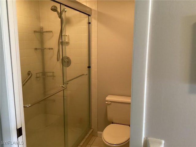 bathroom with tile patterned floors, toilet, and a shower with shower door