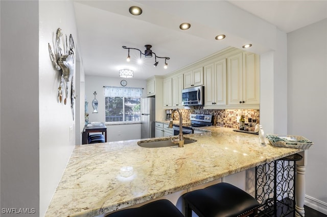 kitchen with sink, appliances with stainless steel finishes, cream cabinets, a kitchen bar, and kitchen peninsula