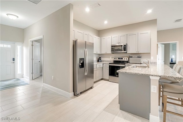 kitchen with appliances with stainless steel finishes, light stone counters, a breakfast bar, sink, and kitchen peninsula