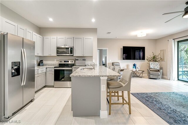 kitchen with a breakfast bar, a center island, light stone countertops, ceiling fan, and appliances with stainless steel finishes