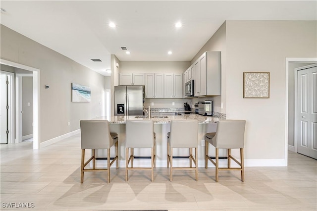 kitchen featuring sink, a breakfast bar, light stone counters, stainless steel appliances, and kitchen peninsula