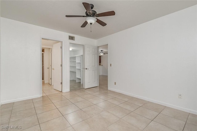 unfurnished bedroom with a walk in closet, a closet, ceiling fan, and light tile patterned flooring